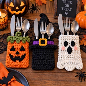 Peut inclure: Trois porte-couverts en crochet aux motifs d'Halloween : une citrouille orange avec une tige verte, un chapeau de sorcière noir avec une bande violette et une boucle jaune, et un fantôme blanc avec des yeux, une bouche noirs et des joues roses.