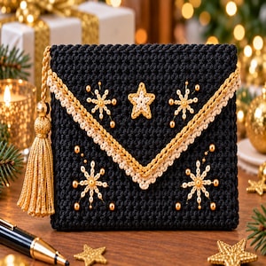 Puede incluir: Un bolso de mano tipo sobre tejido en crochet negro con ribete trenzado dorado y crema, una borla dorada y motivos bordados de estrellas y copos de nieve. La tela texturizada presenta un patrón geométrico con una estrella central.