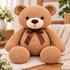 Puede incluir: Un oso de peluche tejido a ganchillo en color marrón claro con un hocico color crema, nariz bordada en marrón oscuro y ojos negros. El oso lleva un lazo de satén marrón oscuro atado al cuello y presenta un acabado de hilo con textura.