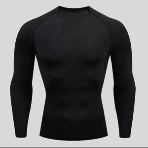 May include: A solid black long-sleeve compression shirt featuring a crew neckline and raglan sleeves. The garment is constructed with a tight-fitting silhouette and visible seam detailing along the shoulders and sides, providing a sleek appearance.