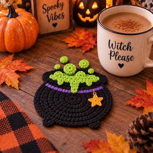 May include: A black crocheted cauldron coaster featuring a purple rim, bright green bubbling liquid, and a small yellow star charm attached to the side. The coaster is circular with a textured yarn finish and a flat, detailed design.