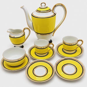 May include: A porcelain tea set featuring a teapot, a creamer, a bowl, and two cups with matching saucers. Each piece is decorated with bright yellow bands, thin black stripes, and gold trim on a white base, creating a cohesive set.