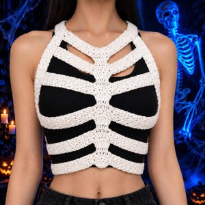 May include: A white crochet rib cage overlay worn over a solid black sleeveless crop top. The white yarn piece features a central vertical spine design with horizontal ribbing extending outward to mimic the structure of a human thoracic cage.