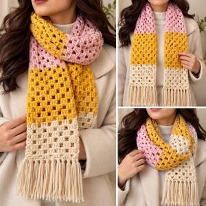May include: A crochet scarf featuring a color-blocked pattern of light pink, mustard yellow, and cream sections. The scarf is constructed with a square-stitch pattern and finished with long, cream-colored fringe tassels at both ends.
