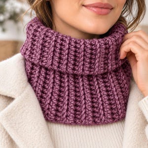 May include: A deep purple, chunky knit cowl neck scarf featuring a prominent vertical ribbed texture. The scarf is worn around the neck, layered over a cream-coloured coat and a matching cream-coloured sweater underneath the outerwear.