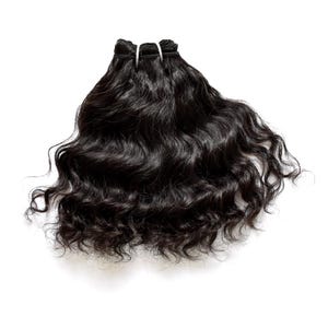 Puede incluir: Un paquete de extensiones de cabello negro oscuro con textura ondulada. El cabello está sujeto en la parte superior con una banda de tejido gruesa y reforzada, permitiendo que los mechones caigan en ondas sueltas y voluminosas con brillo.