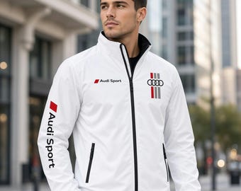 Könnte beinhalten: Eine weiße Jacke mit Reißverschluss und Audi Sport-Logo auf Brust und Ärmel. Das Design umfasst ein schwarzes Innenfutter am Kragen, einen schwarzen Reißverschluss sowie eine vertikale Grafik mit dem Vier-Ringe-Emblem und rot-grau-schwarzen Streifen.