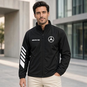 May include: A black zip-up jacket featuring a white Mercedes-Benz star logo on the left chest and the AMG text logo on the right chest. The right sleeve displays a white graphic pattern of diagonal stripes. The jacket has a high collar and pockets.