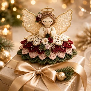 A crochet angel ornament rests atop a wrapped gift box with a gold ribbon against a blurry festive background.