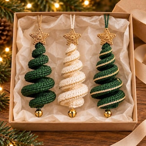 Peut inclure: Un ensemble de trois décorations de sapin de Noël en crochet en forme de spirale dans une boîte cadeau. Deux sapins sont vert foncé et un est blanc, chacun surmonté d'une étoile dorée en crochet avec une petite clochette dorée à la base.