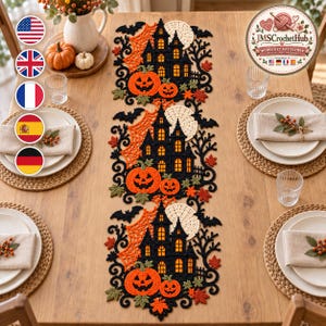 May include: A long, rectangular crochet table runner featuring three repeating motifs of a black haunted house, orange jack-o'-lanterns, a white circular moon, orange spiderwebs, black bats, and scattered autumn leaves in red, orange, and green.