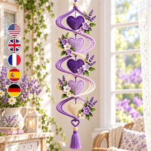 May include: A vertical hanging decoration featuring four crocheted hearts in shades of purple and cream, arranged within a spiraling cream-colored structure. Each heart is accented with small crocheted lavender sprigs and white flowers, ending in a tassel.
