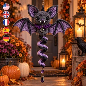 May include: A crocheted hanging bat ornament featuring a dark gray body, purple inner wings, and a purple ruffled collar. It has large black eyes, white fangs, and a silver crescent moon charm. A spiral tail ends in a purple faceted crystal bead.