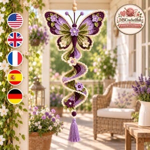 May include: A hanging crochet butterfly ornament featuring purple, green, and cream yarn colors. The butterfly has a spiraling tail decorated with small crocheted flowers and a purple tassel at the bottom. It is suspended by a string with wooden beads.