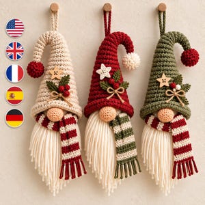Op de afbeelding: Drie hangende gehaakte kabouterornamenten met lange witte baarden. De linker kabouter is crème met een rode pompon, de middelste is rood met een witte pompon en de rechter is olijfgroen met een rode pompon. Elk heeft een houten ster en bessen.