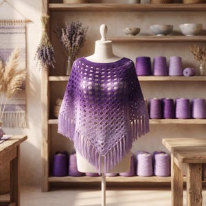 May include: A crochet poncho featuring an ombre color gradient that transitions from deep purple at the neckline to a lighter lavender at the hem. The garment has an open, repeating diamond stitch pattern and is finished with long fringe trim.