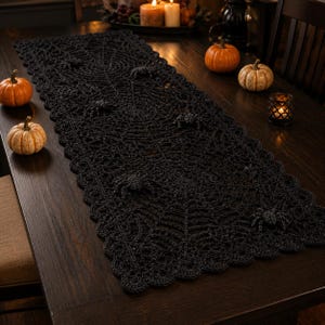 Peut inclure: Un chemin de table rectangulaire en crochet noir présentant un motif complexe de toile d'araignée sur toute la surface et une bordure festonnée. Plusieurs figurines d'araignées noires en relief sont fixées sur le chemin de table.