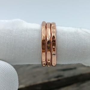 Op de afbeelding: Een set van drie dunne, roségoudkleurige ringen met een gehamerd, getextureerd oppervlak. Elke ring heeft een consistente, smalle bandbreedte en een reflecterende, metalen afwerking die het licht vangt met kleine inkepingen.