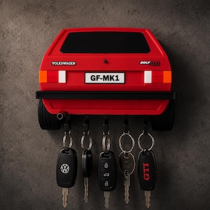 Puede incluir: Un soporte de pared para llaves con forma de parte trasera de Volkswagen Golf GTI rojo, con parachoques negro, luces traseras y una matrícula que dice GF-MK1. Incluye cinco ganchos negros, cada uno con un llavero y llaves de coche.