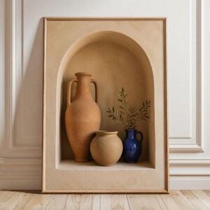 May include: A rectangular wall art piece featuring a beige arched alcove containing three vessels: a tall terracotta amphora, a round tan clay pot, and a small glossy cobalt blue pitcher holding a sprig of green olive leaves.