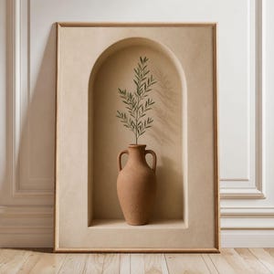 Può includere: Un'opera d'arte murale rettangolare incorniciata che presenta un'alcova ad arco color beige. All'interno dell'alcova si trova un vaso ad anfora color terracotta con due manici, contenente un singolo ramo verde con foglie. La cornice è in legno chiaro.