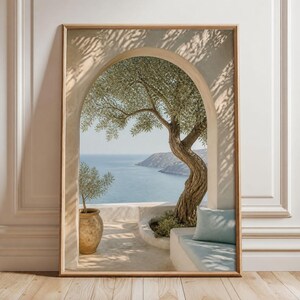 以下が含まれることがあります： 穏やかな青い海を見下ろすアーチ型の石の出入り口を描いた、額装された縦型のウォールアートプリント。節くれだったオリーブの木、テラコッタの鉢、石のベンチに置かれた水色のクッションが、柔らかな日差しの中に表現されています。