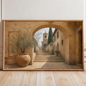 Può includere: Una stampa artistica da parete orizzontale incorniciata che raffigura un arco in pietra mediterraneo che conduce a una scalinata e a un campanile. Un grande vaso in terracotta con un ulivo si trova in primo piano, con toni beige e ocra.