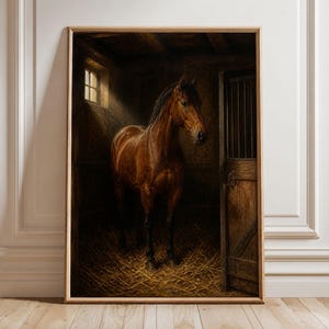 Op de afbeelding: Een ingelijste wandkunstprint met een bruin paard in een donkere houten stal. Het paard wordt verlicht door een enkele lichtstraal die door een klein raam valt. De vloer is bedekt met stro en een houten staldeur is duidelijk zichtbaar.