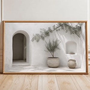 Könnte beinhalten: Ein rechteckiger gerahmter Kunstdruck, der eine weiße Wand im mediterranen Stil mit einem Torbogen, einem kleinen Olivenbaum im Topf, einer Wandnische mit einer Schale und einem kleinen Keramikgefäß zeigt, wobei Zweige Schatten werfen.