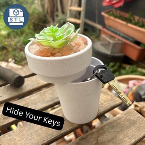 May include: A white speckled cylindrical container with a removable top section holding a green succulent plant and pink salt crystals. A metal key with a black plastic head is inserted into the side of the container, which features the text Hide Your Keys.