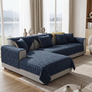 May include: A navy blue sectional sofa cover featuring a quilted square pattern. The cover includes matching navy blue square throw pillows and a yellow throw blanket draped over the backrest, providing a textured layer over the light gray sofa.