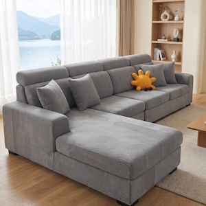 Puede incluir: Un sofá seccional gris cubierto con una tela texturizada que presenta un patrón repetitivo de círculos concéntricos y arcos. El sofá incluye varios cojines grises a juego y un cojín de peluche amarillo brillante con forma de sol y una cara.