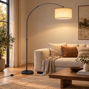 May include: A tall floor lamp with a slender black metal arched pole and a circular black marble base. The lamp features a cylindrical drum shade made of light beige textured fabric that emits a warm, soft glow when illuminated from within.