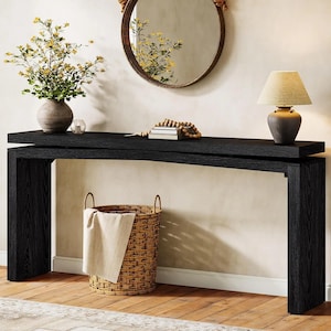 May include: A black wooden console table with a rectangular top and two vertical side supports. On the table sits a gray vase with yellow flowers, a small glass candle holder, a stack of books with wooden beads, and a gray table lamp.