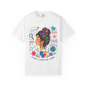 Op de afbeelding: Een wit t-shirt met een kleurrijke afbeelding van een persoon met een bloemrijke knot, omringd door iconen zoals een vergrootglas, een puzzelstuk, een wereldbol en een hart. De tekst bevat de woorden FUNCTION, TEACH, DATA, REINFORCE, GENERALIZE, SCIENCE, COMPASSION en CHANGE.
