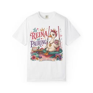 Op de afbeelding: Een wit t-shirt met een afbeelding van een eend met een kroon, hoofdband en ketting, zittend op een schommel met een mok. De tekst luidt La REINA del PAIRING, CONEXIÓN CONFIANZA REFUERZO en PRIMERO CONEXIÓN DESPUÉS CORRECCIÓN.