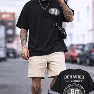 Puede incluir: Camiseta y gorra negras con el logo "BU", combinadas con pantalones cortos color caqui y zapatillas altas. La camiseta presenta un gráfico de cerebro y las palabras "Behavior University". El conjunto se completa con un pequeño bolso bandolera negro.