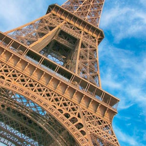 Peut inclure: Une vue en contre-plongée de la structure en treillis de fer brun de la tour Eiffel sur un ciel bleu vif avec des nuages légers. Le texte Accessible Paris et The Complete PRM & Senior Travel Guide est imprimé en blanc en haut à gauche.