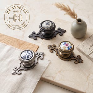 May include: Three decorative cabinet knobs with ornate metal backplates. One knob features a blue and white wave pattern, another a floral design, and the third a geometric star motif. The Brasselle Home logo is visible in the upper left corner.