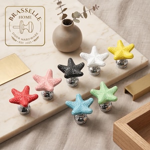 Puede incluir: Un conjunto de siete pomos para armarios con forma de estrella de mar en rojo, rosa, negro, blanco, amarillo, azul claro y verde claro, con superficie texturizada y base de metal plateado pulido, con el logotipo de Brasselle Home.
