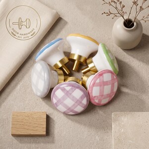 May include: A collection of six ceramic cabinet knobs with a rounded shape, featuring hand-painted plaid patterns in blue, yellow, green, grey, purple, and pink. Each knob has a gold-toned metal base and a smooth, glossy white finish.