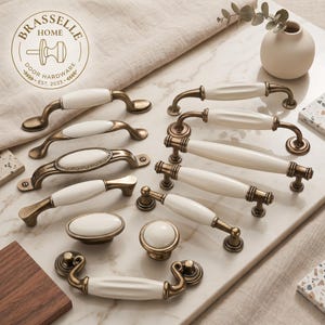 May include: A collection of cabinet hardware including various drawer pulls and knobs with antique brass metal finishes and white ceramic centers. The set features diverse shapes, including curved, straight, and oval designs, with one pull displaying a Greek key pattern. A logo for Brasselle Home Door Hardware Est. 2023 is visible.