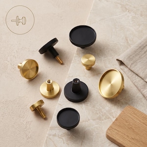 Peut inclure: Une collection de boutons de placard circulaires aux finitions noir mat et or brossé. Les boutons présentent une face plate et ronde avec une tige centrale et une vis métallique filetée pour l'installation. Certains sont vus de face, d'autres de dos.