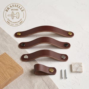 May include: Three arched dark brown leather drawer pulls with metallic fasteners in brass, black, and silver finishes, plus one folded leather loop pull with a brass fastener, two silver screws, and a small square marble tile with the Brasselle Home logo.