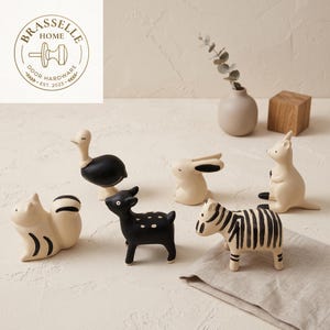 May include: A collection of six animal-shaped cabinet knobs featuring a squirrel, ostrich, deer, rabbit, kangaroo, and zebra. Each knob is crafted in a cream and black color palette. The Brasselle Home Door Hardware logo is visible in the corner.
