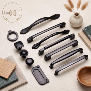 Könnte beinhalten: Eine Sammlung von mattschwarzen Schrankbeschlägen, darunter verschiedene Schubladengriffe, Griffe und Knöpfe. Das Set bietet eine Mischung aus geschwungenen, geraden und ringförmigen Designs, alle in einer soliden schwarzen Farbe gehalten.