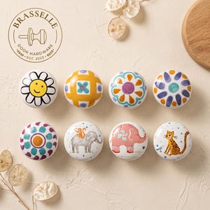 Può includere: Otto pomelli rotondi in ceramica per mobili con vari disegni, tra cui una margherita gialla, motivi geometrici, un elefante grigio con una scimmia, un elefante rosa e un leopardo. Il logo BRASSELLE DOOR HARDWARE EST. 2023 è stampato in alto a sinistra.