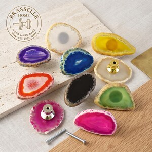 Könnte beinhalten: Eine Sammlung von zehn Schrankknöpfen aus Achatstein in verschiedenen Farben, darunter Violett, Blau, Orange, Schwarz, Grün, Pink, Gelb und Weiß. Jeder Knopf besteht aus einer natürlichen Steinscheibe mit einem metallischen Befestigungsbolzen.