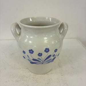 Könnte beinhalten: Ein weißer Keramiktopf mit zwei seitlichen Griffen und einem blauen Blumenmuster auf der Vorderseite. Das Design besteht aus kleinen blauen Blüten mit Stielen und Blättern, die in einem Bündel auf dem bauchigen Gefäß angeordnet sind.
