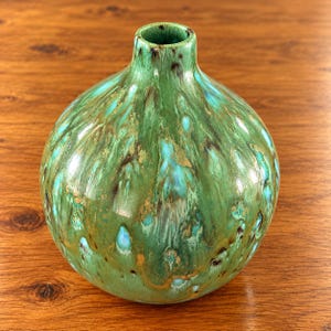 May include: A spherical ceramic vase with a narrow neck and a glossy finish. The surface features a variegated glaze in shades of emerald green, turquoise, and dark brown, creating a flowing, dripped pattern across the rounded body.